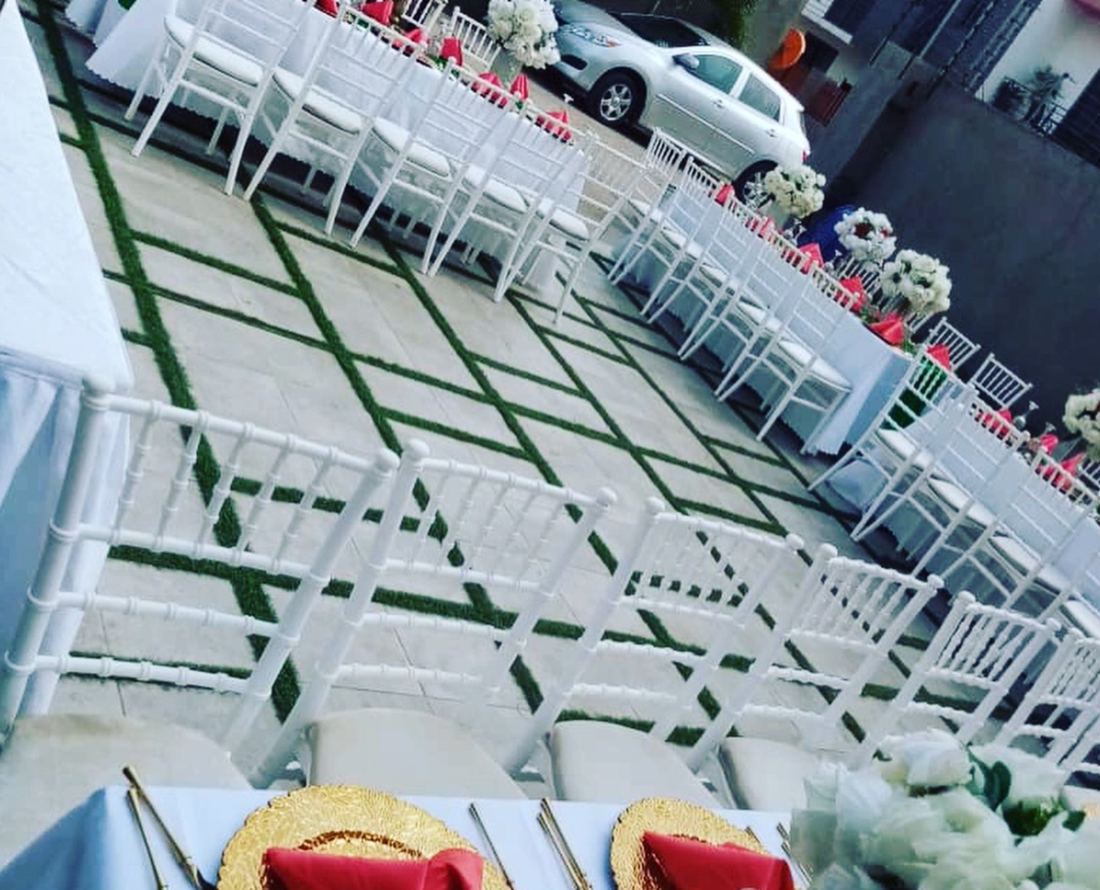 Long rows of white banquet chairs and set tables with white floral centrepieces across a paved courtyard with grass lines