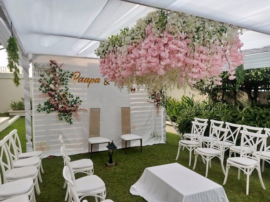Ceremony set-up under a white canopy with a large hanging cloud of pink and white blossoms over a white backdrop, two gold and white chairs and a floral spray
