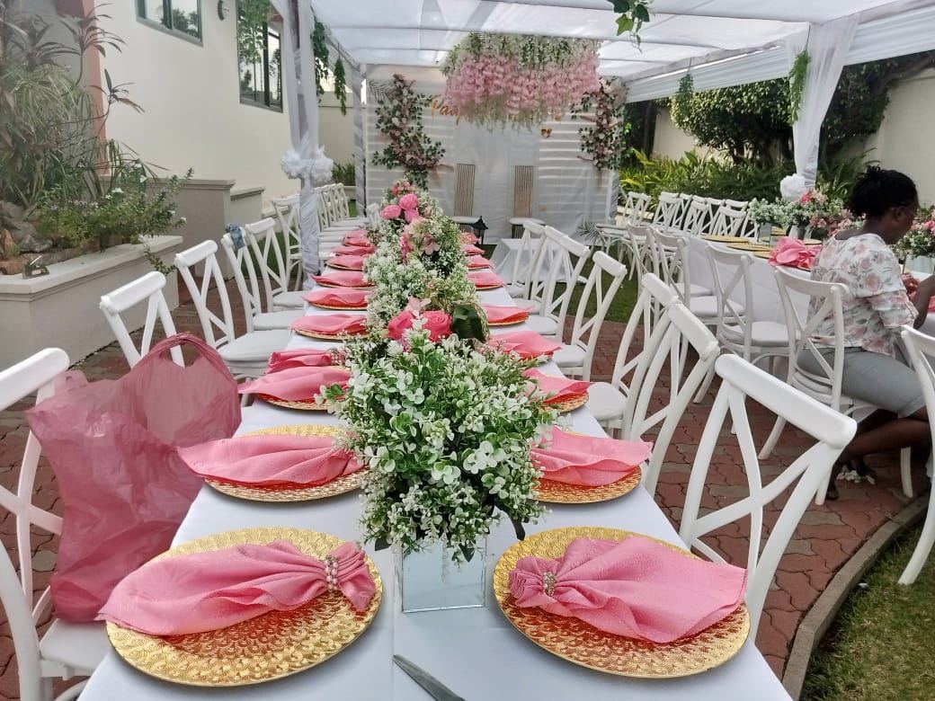 Outdoor table with pink napkins on gold chargers and a low arrangement of white and pink flowers, under a white canopy with hanging pink blossoms