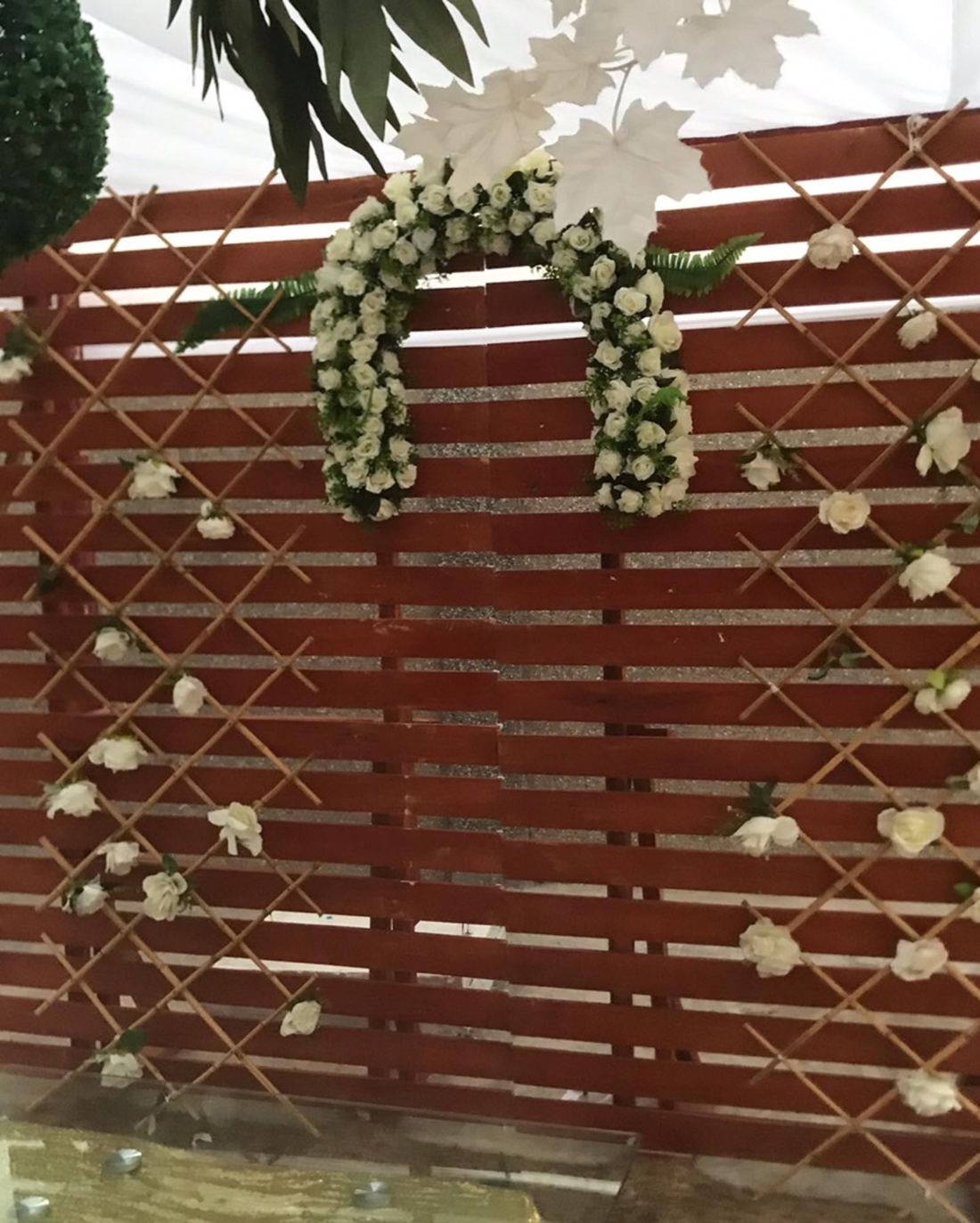 Dark wooden slat backdrop with bamboo lattice, scattered white roses and an arch of white roses with hanging white leaves